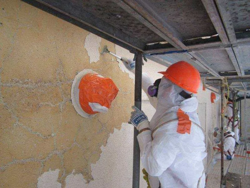 AES crew member in a protective suit and orange hard hat removing wall material from scaffolding