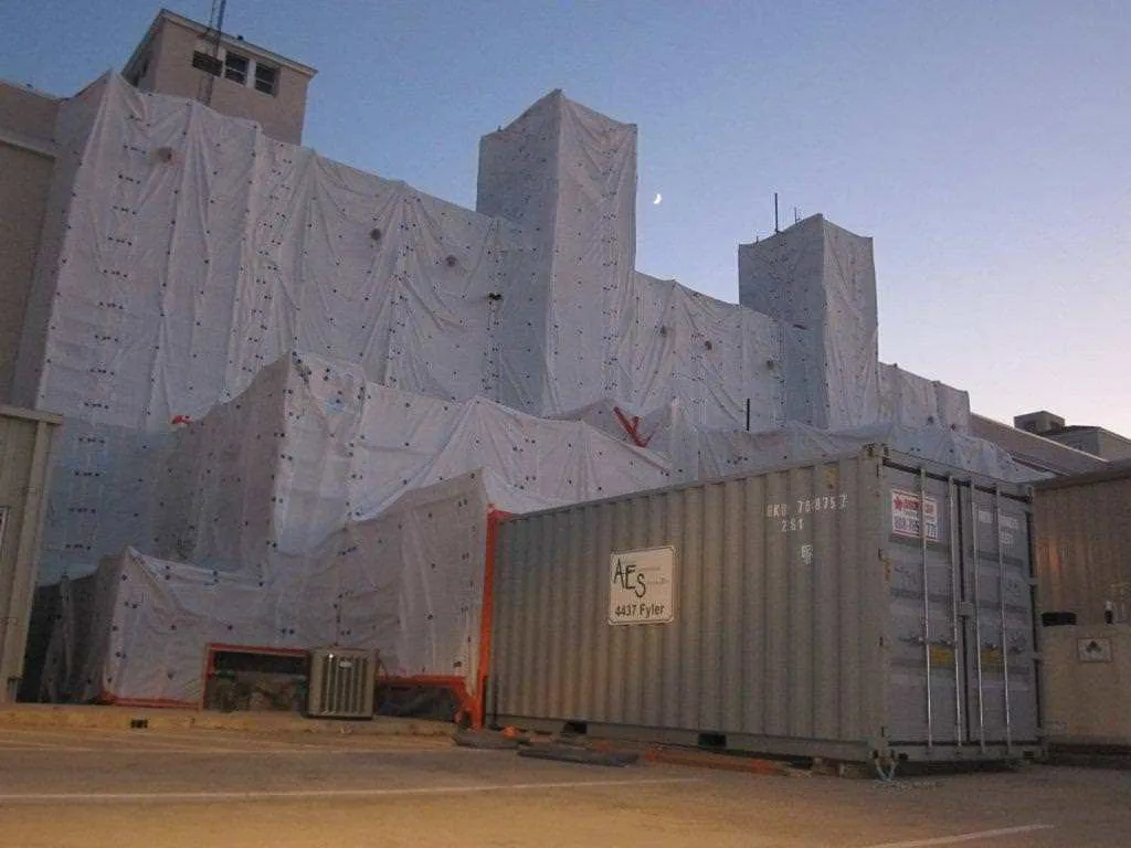 Building wrapped in white containment sheeting with an AES storage container in front